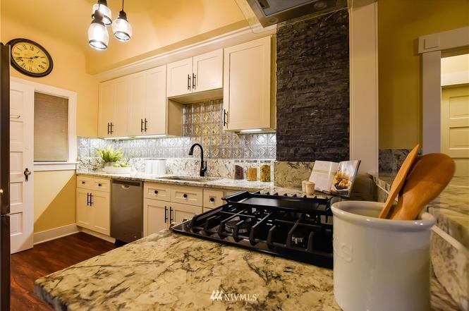 Renovated kitchen with granite island, gas range, and tin backsplash